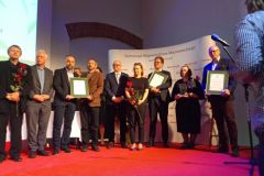 Kilku osób pozuje do zdjęcia z nagrodami. W tle ekran teatrowy