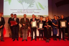 Kilku osób pozuje do zdjęcia z nagrodami. W tle ekran teatrowy