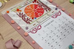 Ręcznie wykonany kalendarz zdobiony wycinanką kurpiowską, tasiemkami i różyczkami dekoracyjnymi