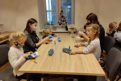 Dzieci oraz dwie kobiety siedząc przy stole wykonują zabawki z papieru.