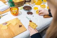 Dziewczynka dekoruje goździkami bombkę w kształcie choinki z wosku pszczelego.