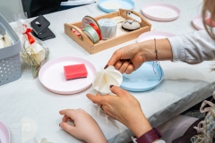 Ręce kobiety wykonującej bombkę z opłatka moczonego wodą, w tle widać talerzyk z gąbką i wodą.