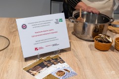 Na stole stoi niewielka tabliczka informacyjna oraz leżą ulotki