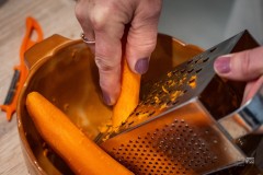 Dłonie osoby ucierającej marchew na metalowej tarce