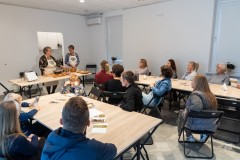 Sala, w której odbywa się prezentacja przygotowania potrawy. Kilkanaście osób siedząc przy stołach przygląda się pracy dwóch twórczyń.