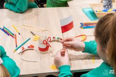 Dłonie dziecka siedzącego przy stole trzymające małą, papierową  flagę