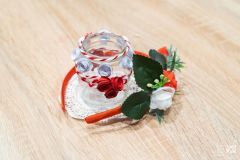 Na stole szklany lampionik z biało-czerwoną dekoracją, wokół niego czerwona opaska na włosy udekorowana biało-czerwonymi kwiatkami i zielonymi listkami.