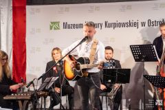 Mężczyzna z gitarą oraz w tle inni muzycy na scenie