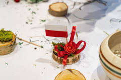 Dekoracja patriotyczna z miniaturową biało-czerwoną flagą, wstążeczkami, różyczką i odrobiną mchu osadzonych na kawałku drewna.
