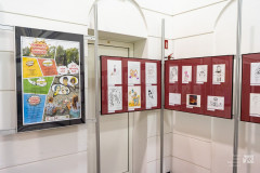 Fragment wystawy rysunków komiksowych. Z lewej strony plakat reklamujący Ostrołęckie Spotkania Komiksowe i wystawy.