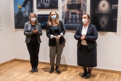 Trzy kobiety w maseczkach stoją na tle fotografii wiszących na ścianie sali wystawowej.