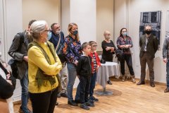 Powyżej dziesięciu osób, w tym dwoje chłopców zwróceni w jednym kierunku stoją w pomieszczeniu sali wystawowej.