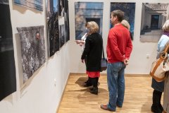 Kilka osób ogląda fotografie wiszące na ścianie w sali wystawowej.