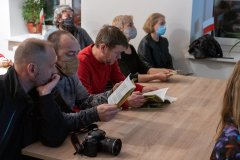 Sześć osób siedzi przy stole, zwróceni w prawą stronę kadru. Widok z boku. Niektórzy trzymają w dłoniach przewodnik.