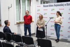 Mężczyzna i dwie kobiety stoją przed widownią. Mężczyzna przemawia. W tle ścianka z logami marki Mazowsze oraz  MKK