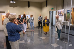 Uczestnicy wernisażu stoją w sali wystawowej, w tle dzieła malarskie
