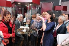 Goście zwiedzają wystawę zabytkowej biżuterii eksponowanej w szklanych gablotach
