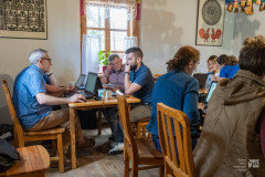Uczestnicy edytonu zebrani w kurpiowskiej izbie, siedzą przy stołach korzystając z komputerów