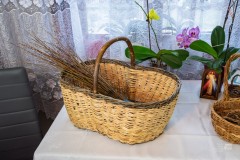 Na stole stoi duży koszyk z wikliny, w którym leży pęk wiklinowych gałązek