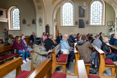 Uczestnicy spaceru wewnątrz kościoła siedzą w ławkach, widok na lewą nawę boczną
