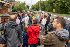 Uczestnicy podczas spaceru, słuchają przemówienia prowadzącej przy jednym z budynków