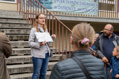 Uczestnicy podczas spaceru, słuchają przemówienia prowadzącej przy jednym z budynków