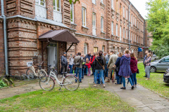 Uczestnicy podczas spaceru, słuchają przemówienia prowadzącej przy jednym z budynków
