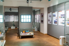 Ogólny rzut na salę wystawową. Gabloty z eksponatami, plansze na ścianach, tablica podświetlana, siedzisko z tektury