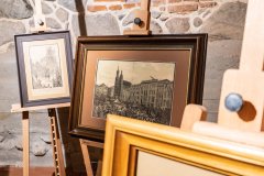 Na sztalugach dwie czarno-białe ilustracje przedstawiające tłum ludzi, ludzi na koniach, budynki. Przy prawej, dolnej krawędzi kadru fragment trzeciej ramy.