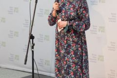 Kobieta stoi, przemawia do mikrofonu. W tle ścianka z logotypami oraz napisem Muzeum Kultury Kurpiowskiej.