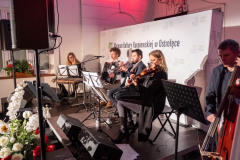 Muzycy siedząc grają scenie. Widok z boku sceny.