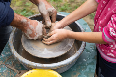 Dłonie twórcy ludowego oraz dziecka tworzą naczynie z gliny