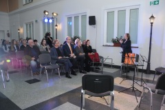 Grupa ludzi słucha kobiety mówiącej przez mikrofon.