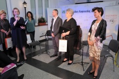 Grupa kilkorga ludzi stoi, kobieta odbiera nagrodę.
