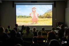 Na ekranie w ciemnej sali wyświetlony film animowany. Przed ekranem widownia