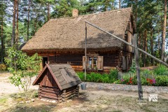 Drewniana chata w Zagrodzie Kurpiowskiej w Kadzidle, przed nią stara, kryta studnia z „żurawiem”