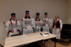 Pięć kobiet w strojach kurpiowskich siedzi przy wspólnym stole. Prezentują firanki z papieru.