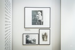 Fragment wystawy, trzy czarno-białe fotografie w ramkach na ścianie, na lewej ścianie fragment nadrukowanego tekstu